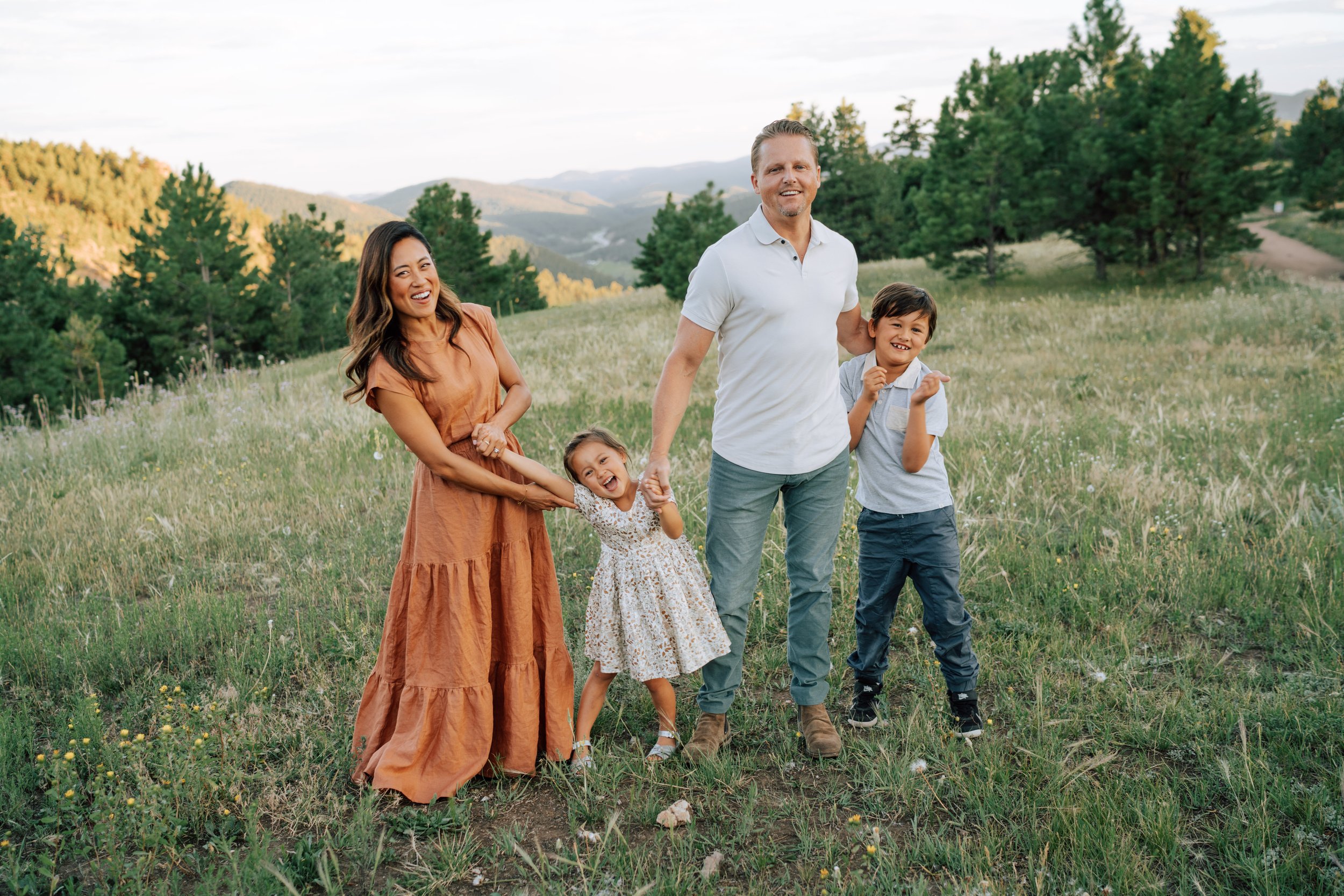 Parents and two children laughing together in an open mountain meadow during a relaxed Colorado family photo session.