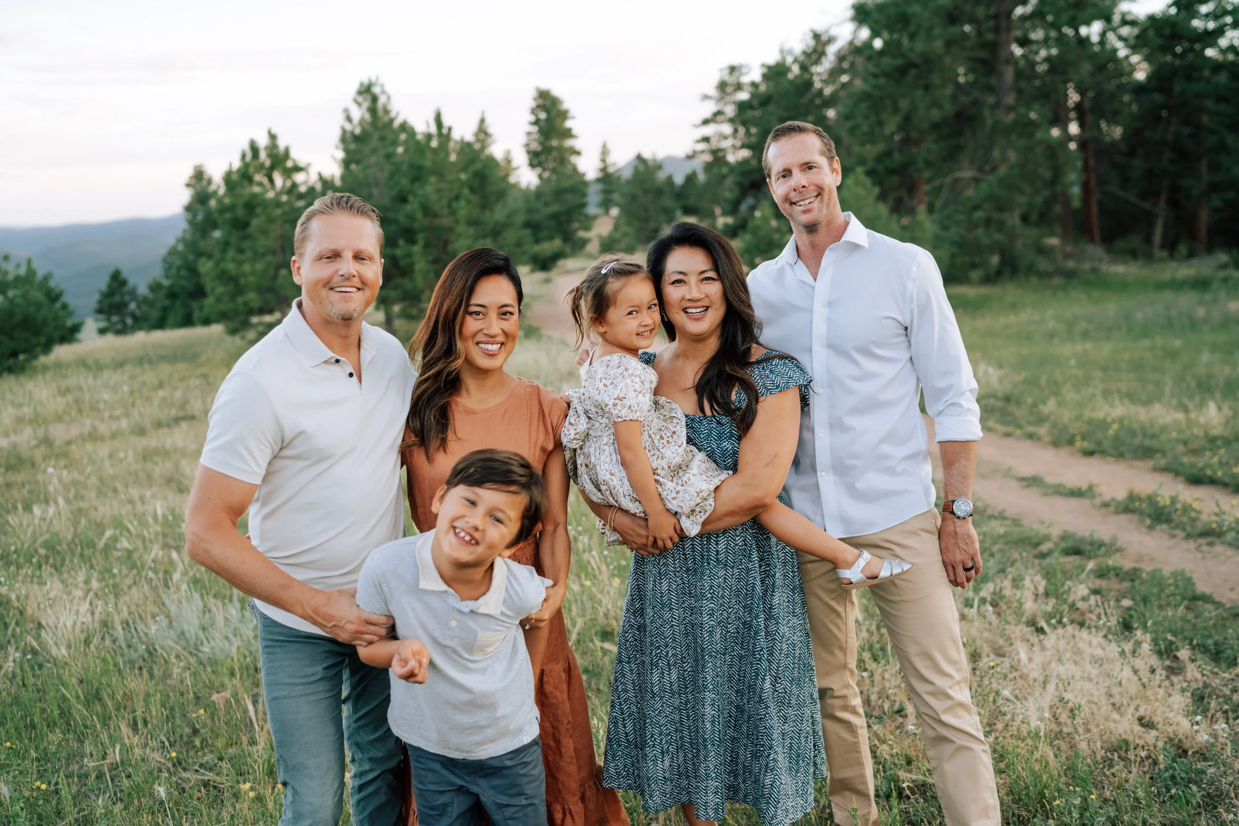 Two families laughing together in an open mountain meadow with pine trees and Front Range scenery behind them.