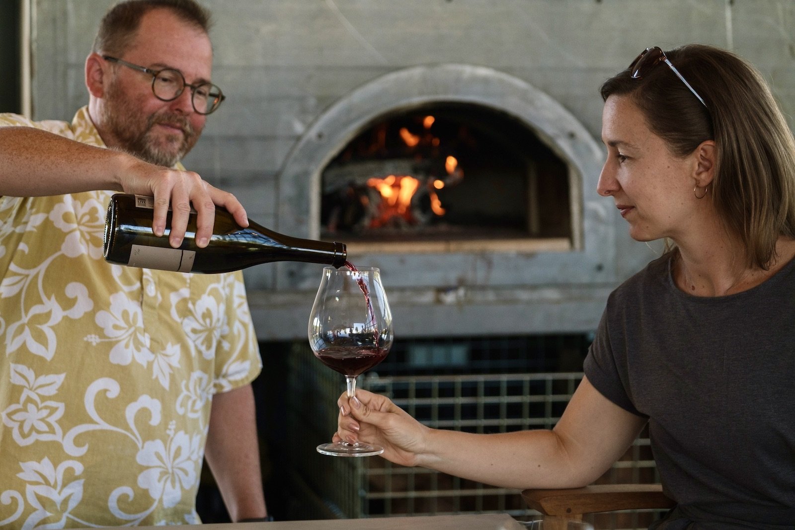 Guest being poured wine in front of the pizza oven