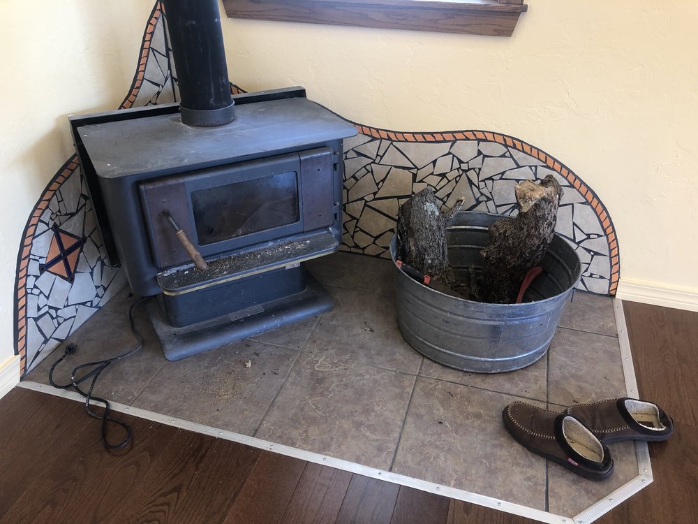 A wood stove on a tiled hearth beside a bucket of kindling