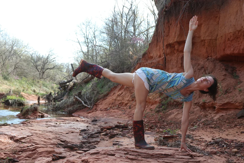 A yogi balancing in half moon pose on red sandstone by the creek