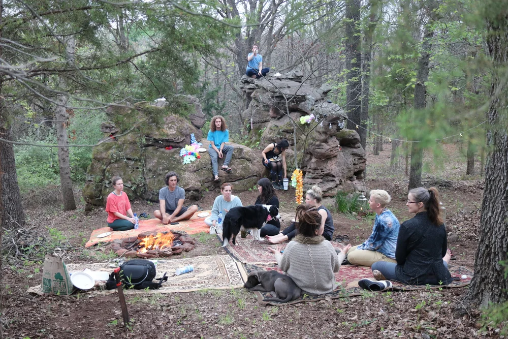 A group practicing on blankets in the forest below a stone outcrop
