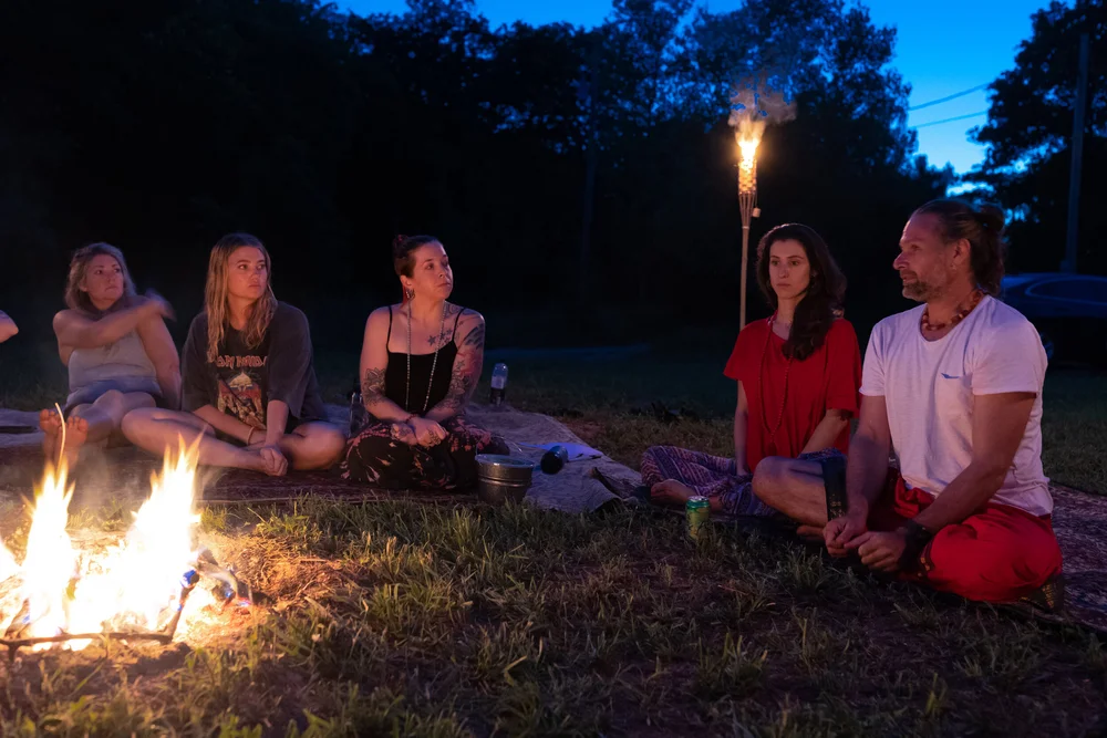A group seated around a fire at night, torches burning behind them