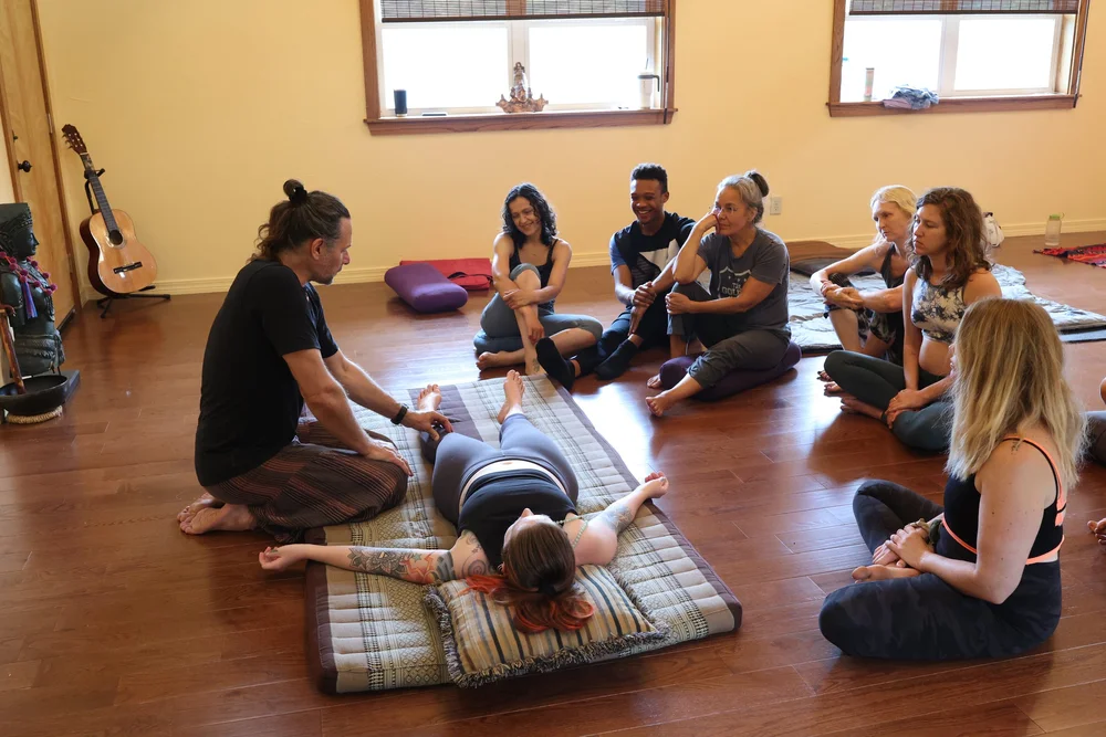 Andrew Eppler demonstrating Thai bodywork on a mat while a circle of students watches