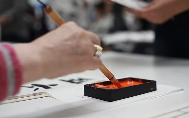 Une main utilisant un pinceau pour faire de la calligraphie sur une feuille avec de l'encre noire.