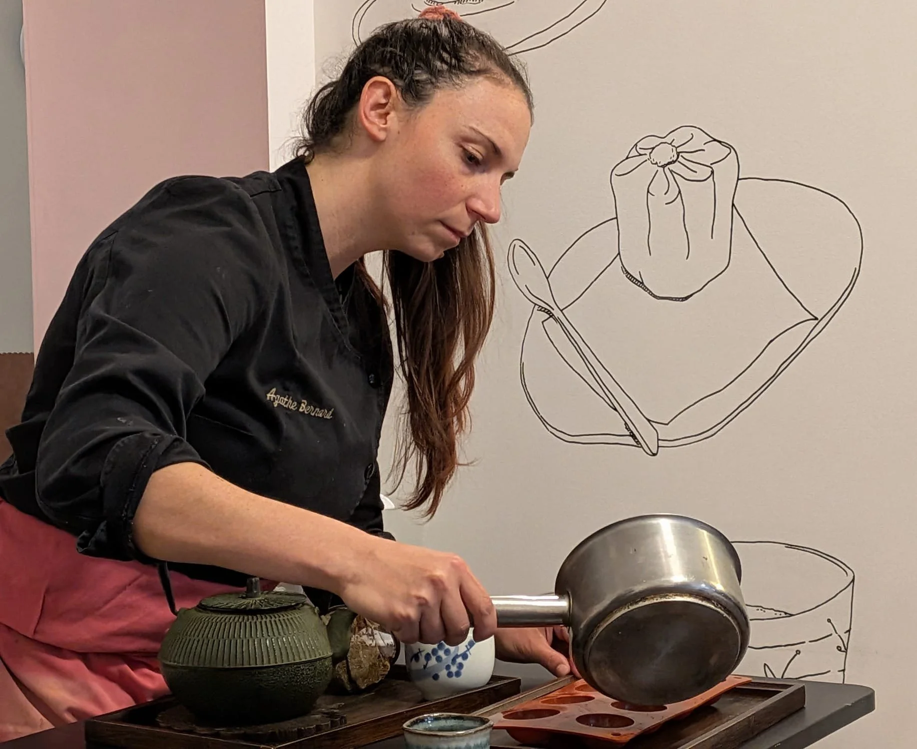 Une femme en uniforme de cuisine verse de l'eau dans un moule à glaçons sur un plan de travail.