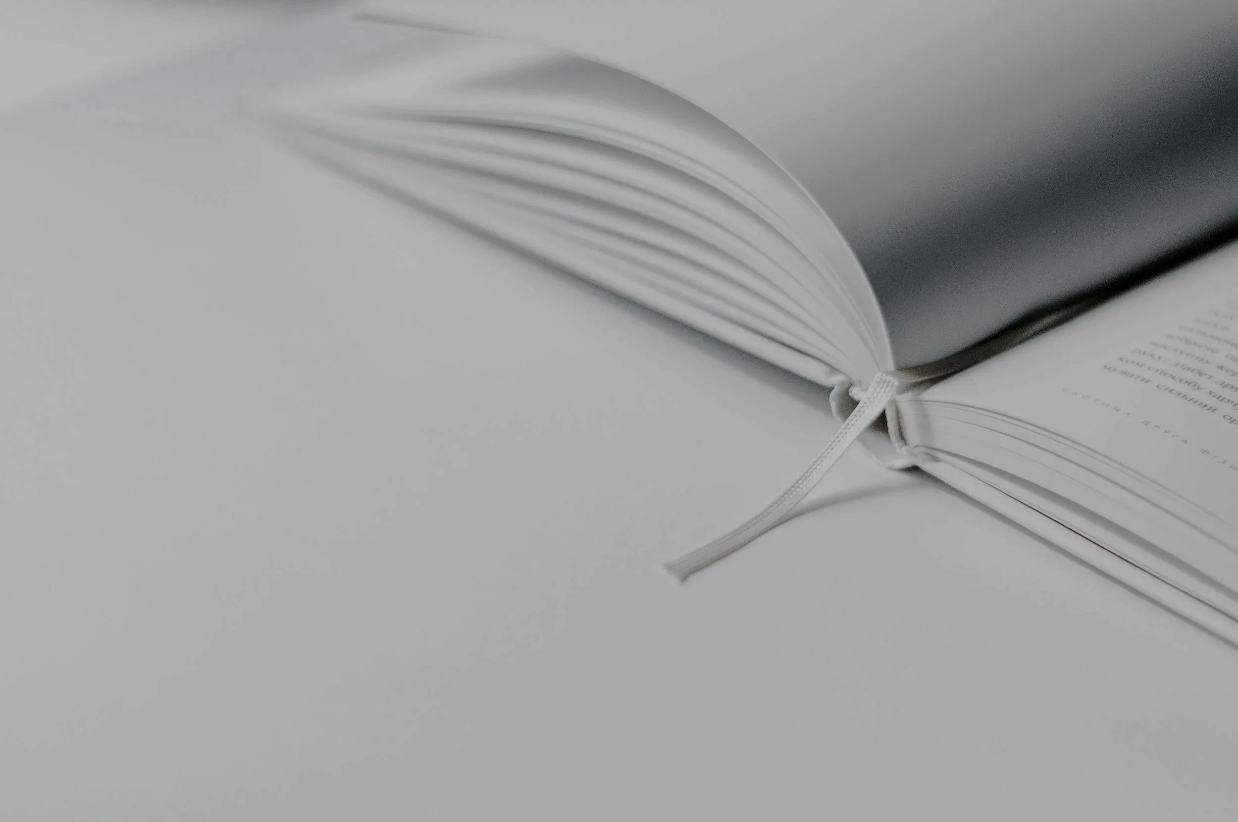 Open white book with a ribbon bookmark on a plain light surface