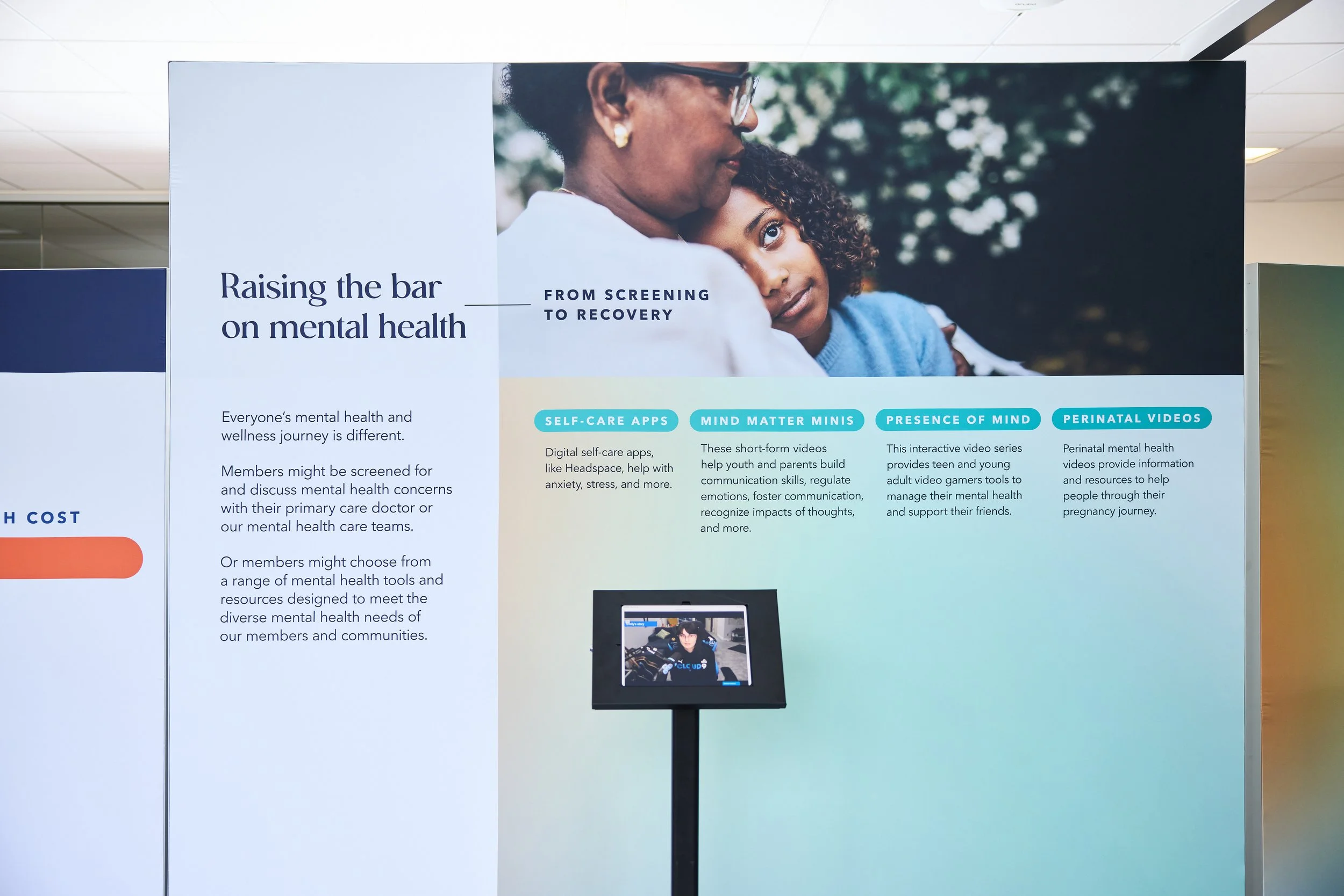 A large informational display board with a photo of a woman and a girl with curly hair, along with text about mental health resources and programs.