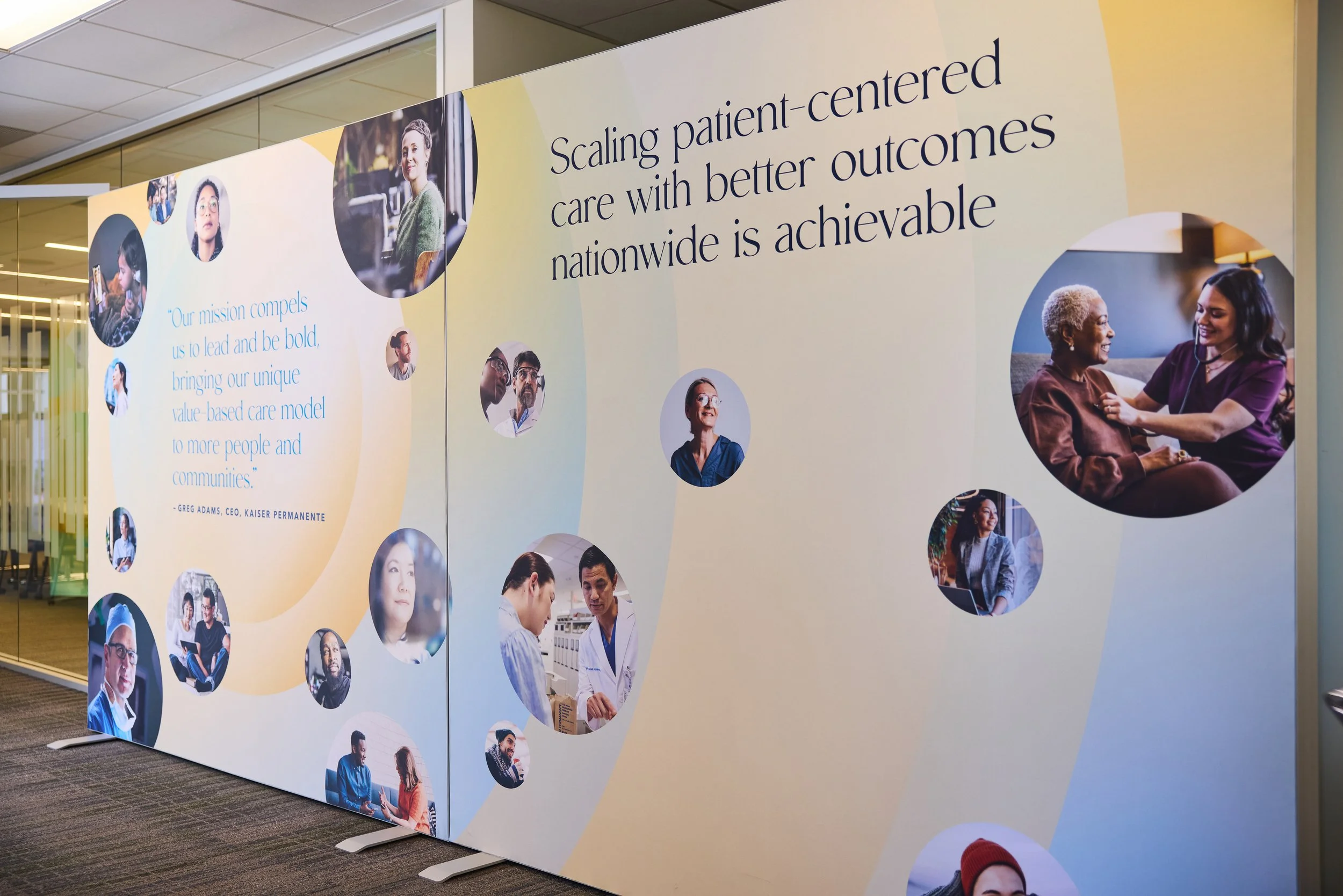 Large display wall with a healthcare or medical theme, featuring images of diverse healthcare professionals and patients, and text emphasizing patient-centered care and outreach.