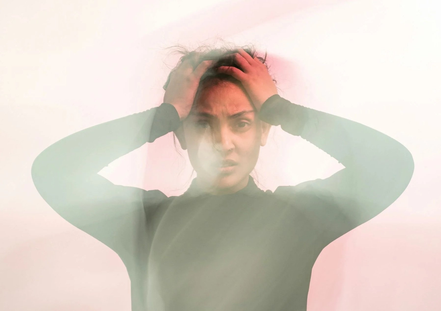 A woman with dark hair holding her head with both hands, looking worried or stressed, with a plain light background.