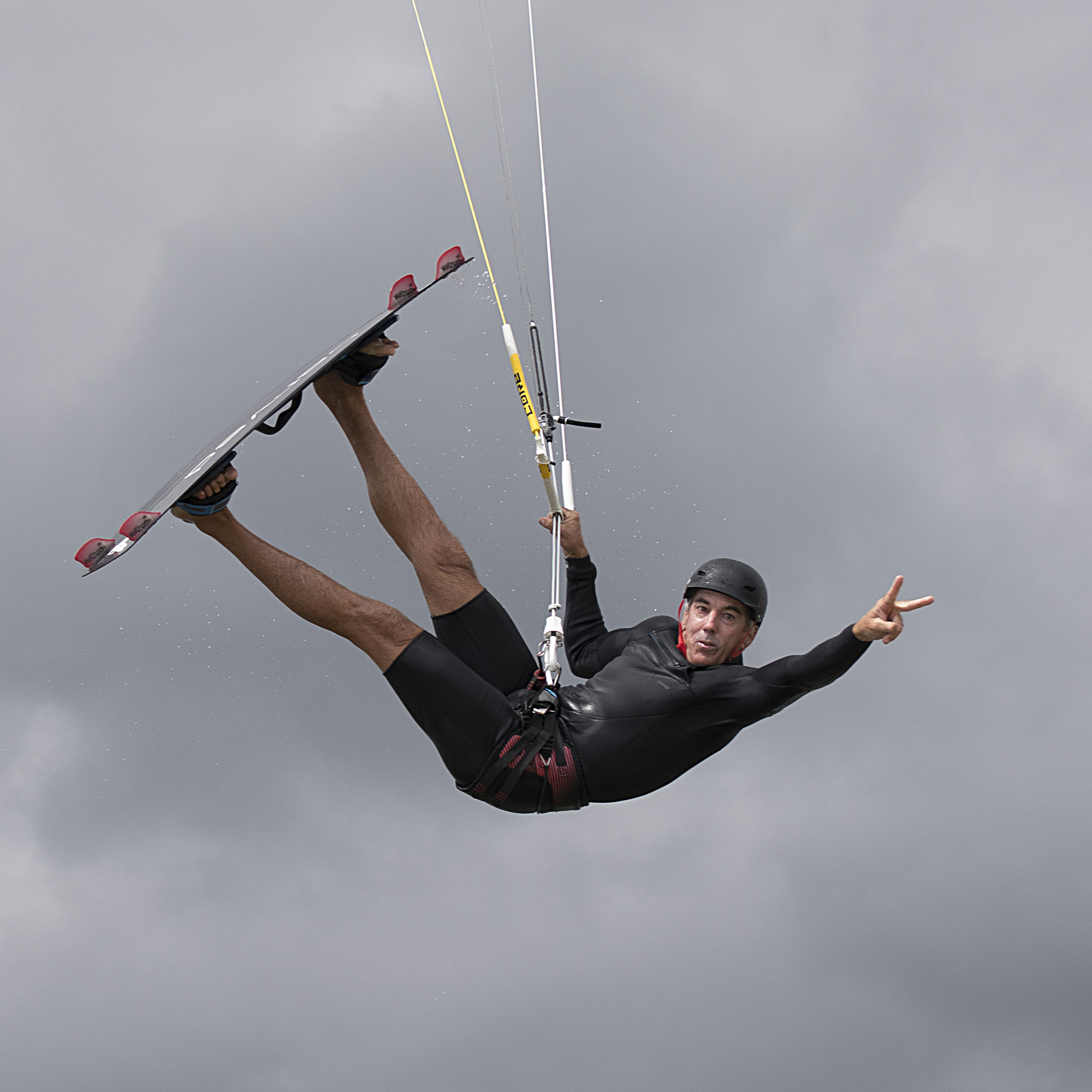  Nevin Sayre gives a peace sign in the middle of a kiteboarding jump on Sengekontacket Pond, Martha’s Vineyard.  