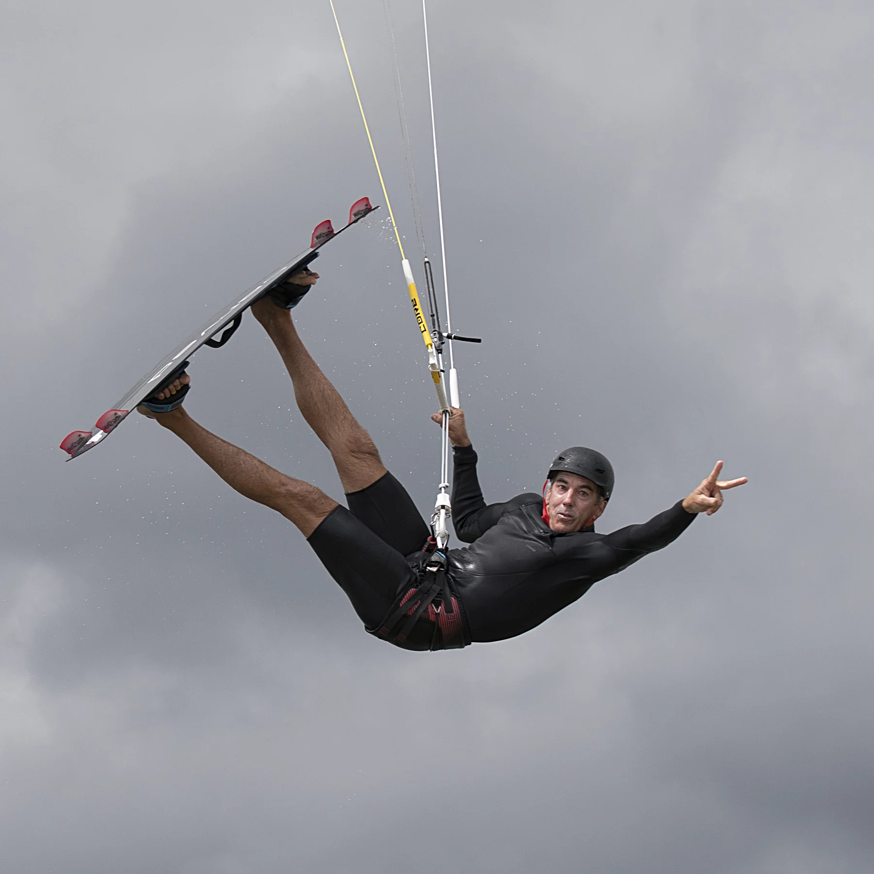 Nevin Sayre gives a peace sign in the middle of a kiteboarding jump.