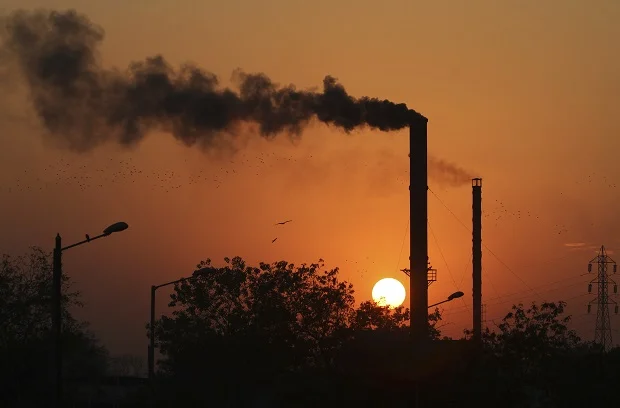 Birds fly past at sun set as smoke emits from a chimney at a factory in Ahmadabad, India, Monday, Dec. 8, 2014. Credit : AP