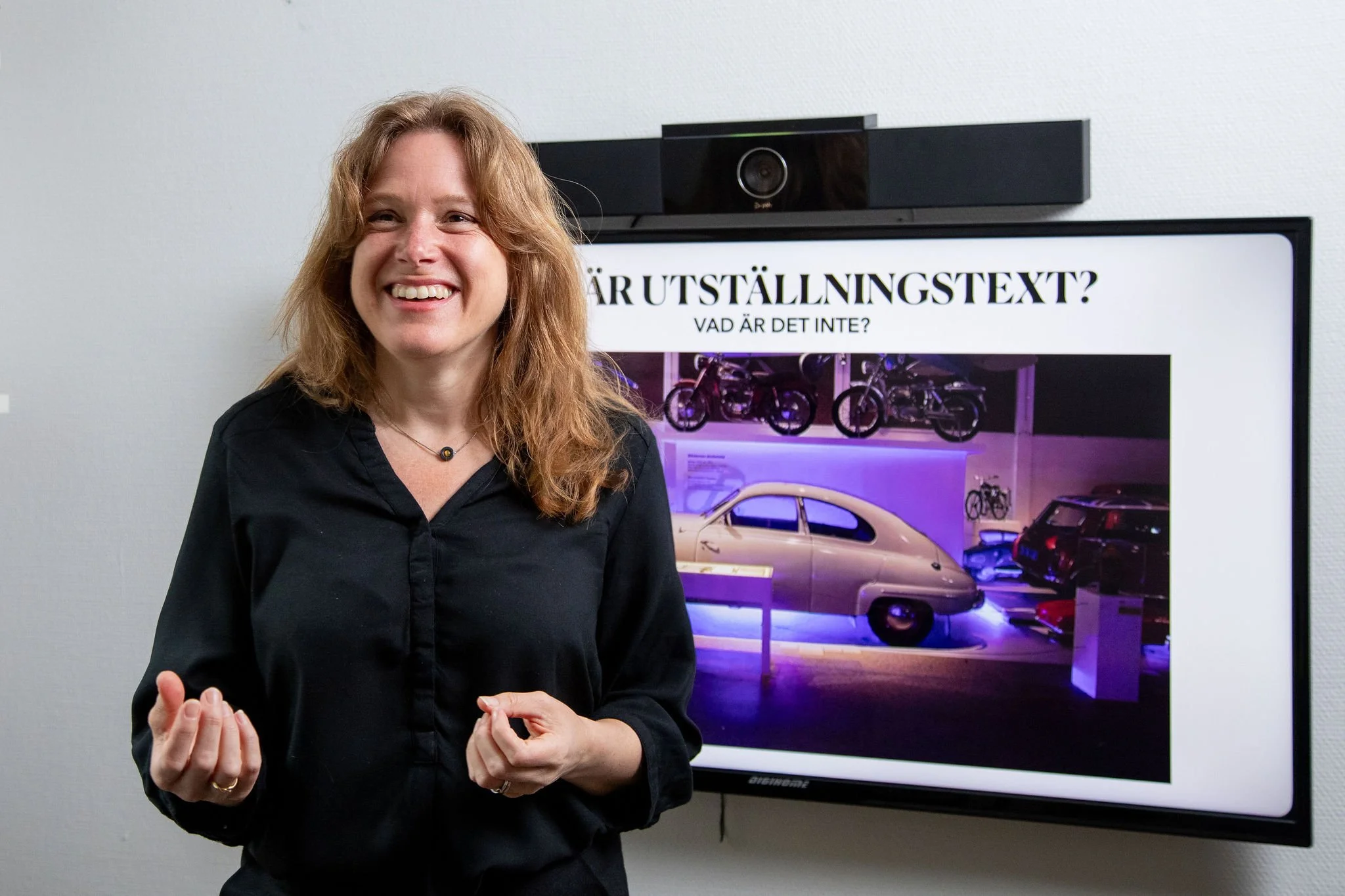 Porträtt av Sofie Bergkvist framför en skärm med texten Vad är utställningstext?