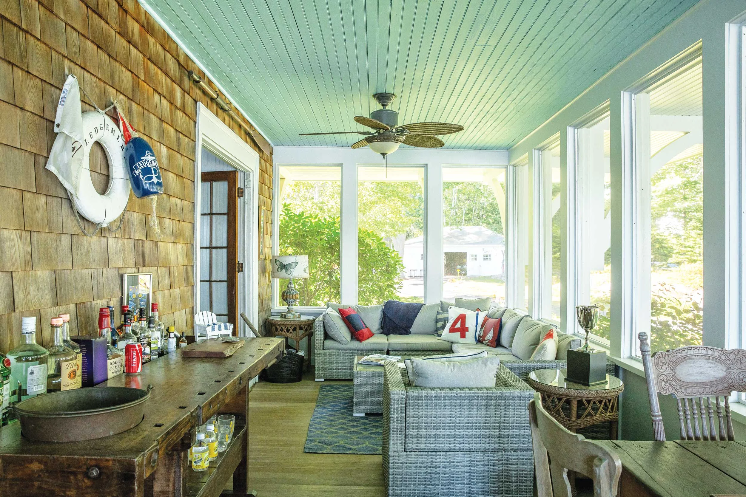 An enclosed porch with a yacht club lifesaver, bar area, game table, and blue ceiling, the latter a custom in South Carolina (where the tradition seems to have to do with warding off evil spirits) and in New England (where the custom may have to do with fooling insects into not building nests.) Other theories about why people paint porch ceilings blue? It resembles the sky.