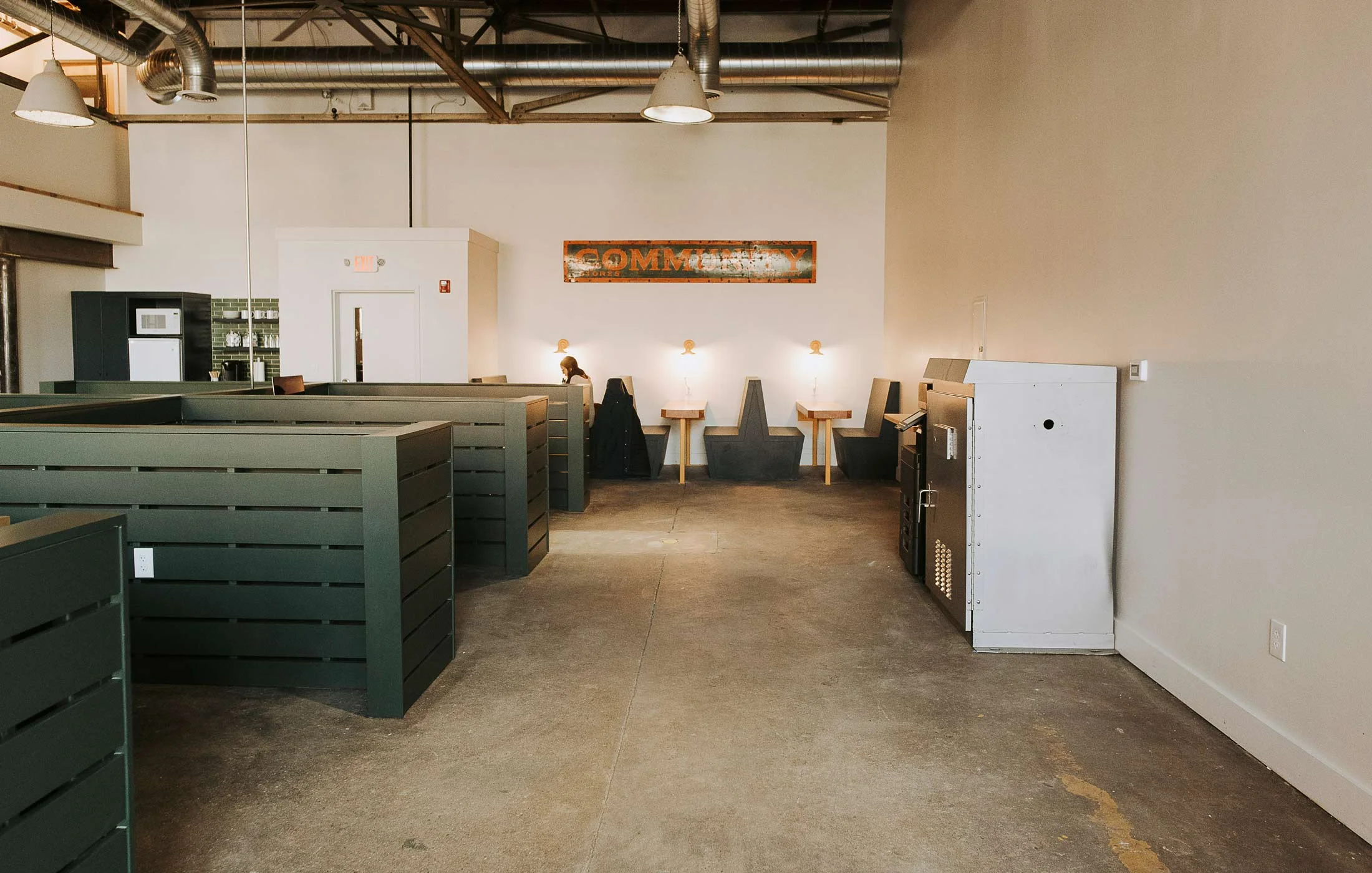 The Public Works’ communal workspace features private offices, open studios, and floating desks. The metal cabinet on the right is a former traffic signal controller and now contains printing paper and supplies. The vintage industrial pendant lights are from Halogen Particle. The “Community” sign was found at Portland Flea-for-All.