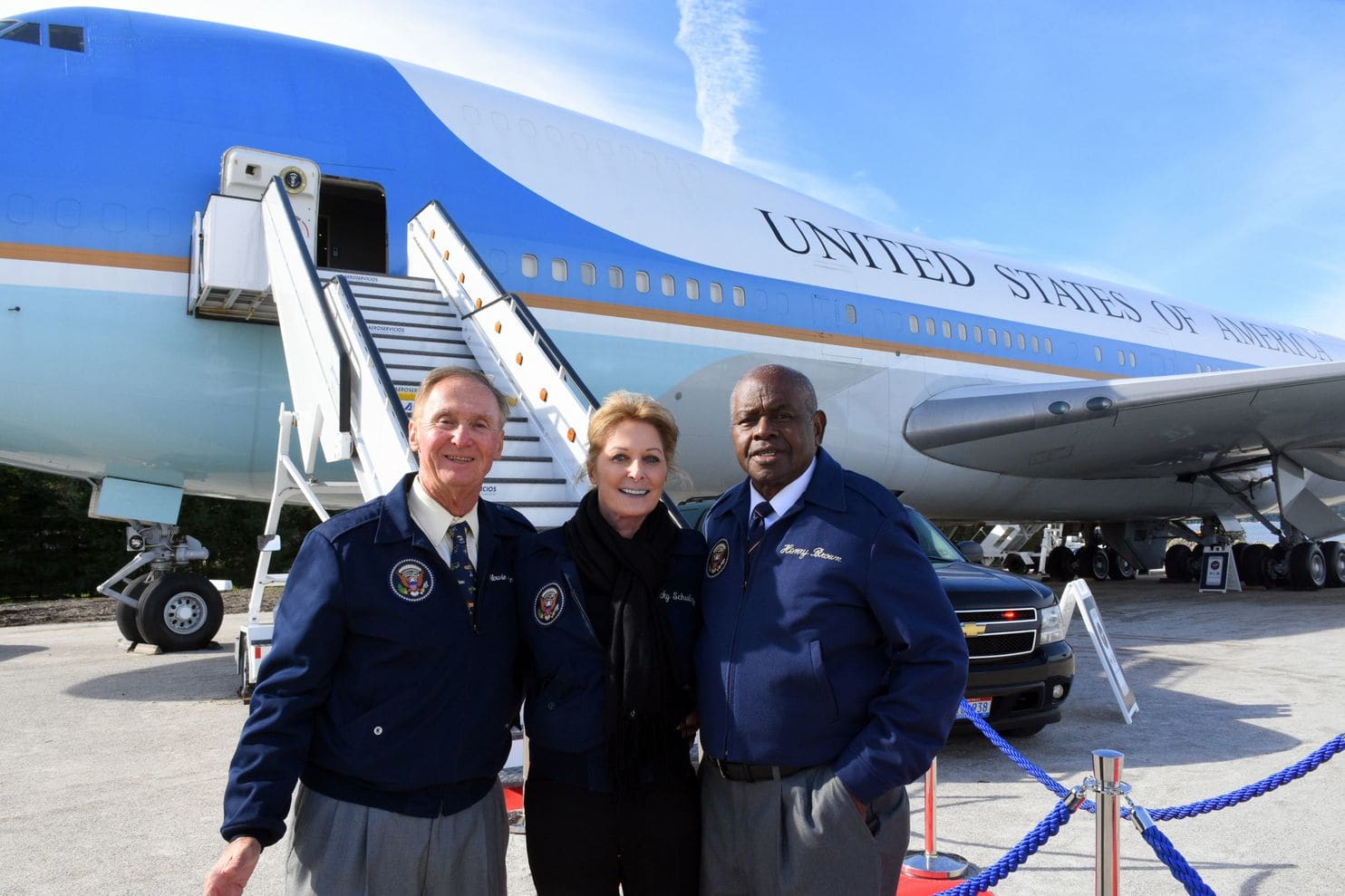 Air Force One flight attendants, from left, Howie Franklin, Becky Schulz and Henry Brown have more than 30 years of service aboard Air Force One among them. They are posing in front of the copy of the airplane at National Harbor. (Ann Cameron Siegal