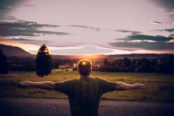 man holding arms out to the side, with yellow light on back of his head