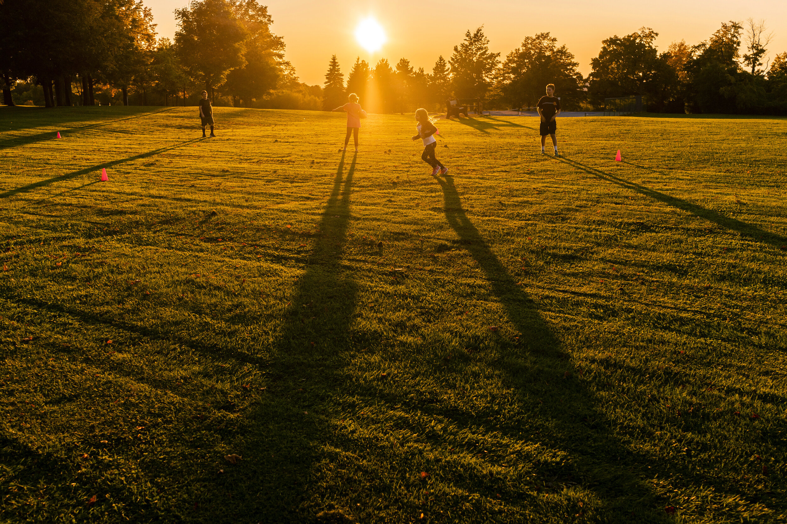 Long shadows stretch across the field as, from left to right, Connor Lamica, 10, Flora Bates, 9, Kate Lamica, 6, and Nicolas Bates, 12, play kickball at Thompson Park.