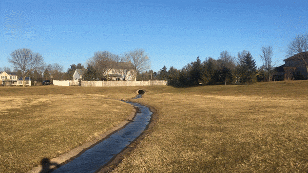 Figure 3. An example of a traditional, grass-lined stormwater detention basin. In this GIF, water enters at the inlet and flows through a concrete channel toward the outlet. In heavy rain, the water will overflow the concrete channel and will be held in the large excavated area.