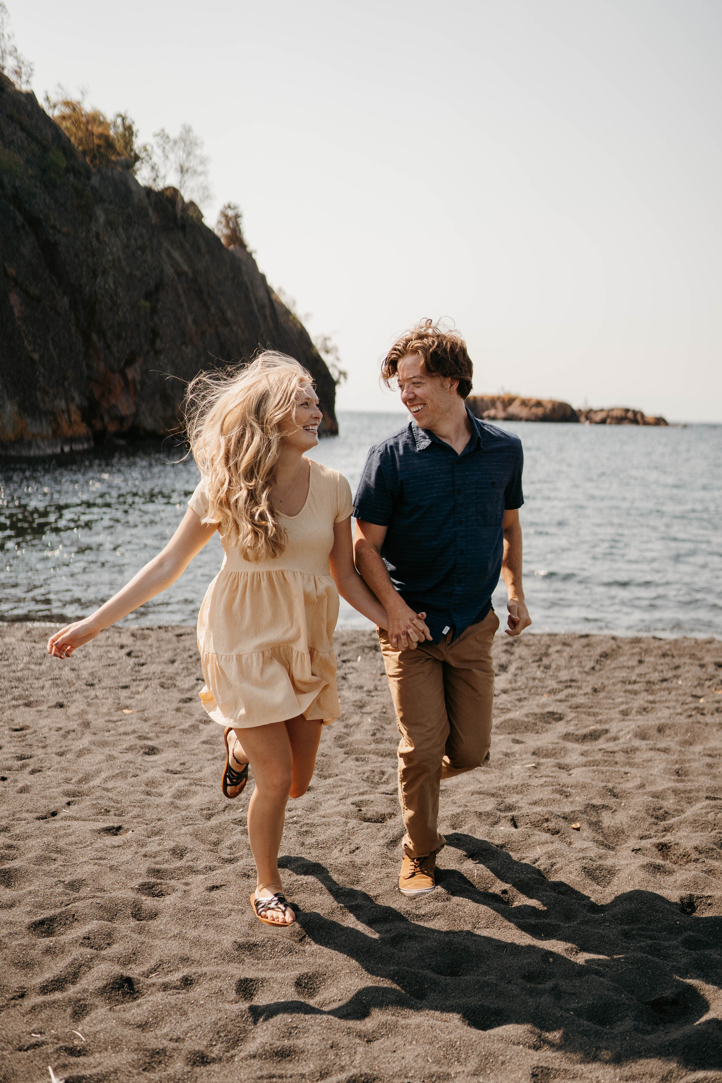 Engaged couple running on black sand beach during their engagement photography session