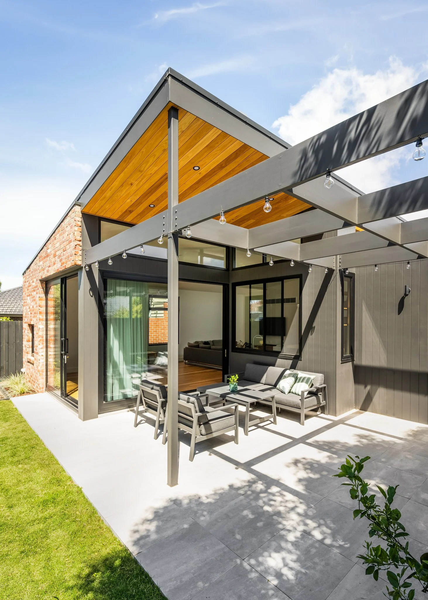 Modern house with an outdoor patio featuring patio furniture and string lights, adjacent to a well-maintained lawn.