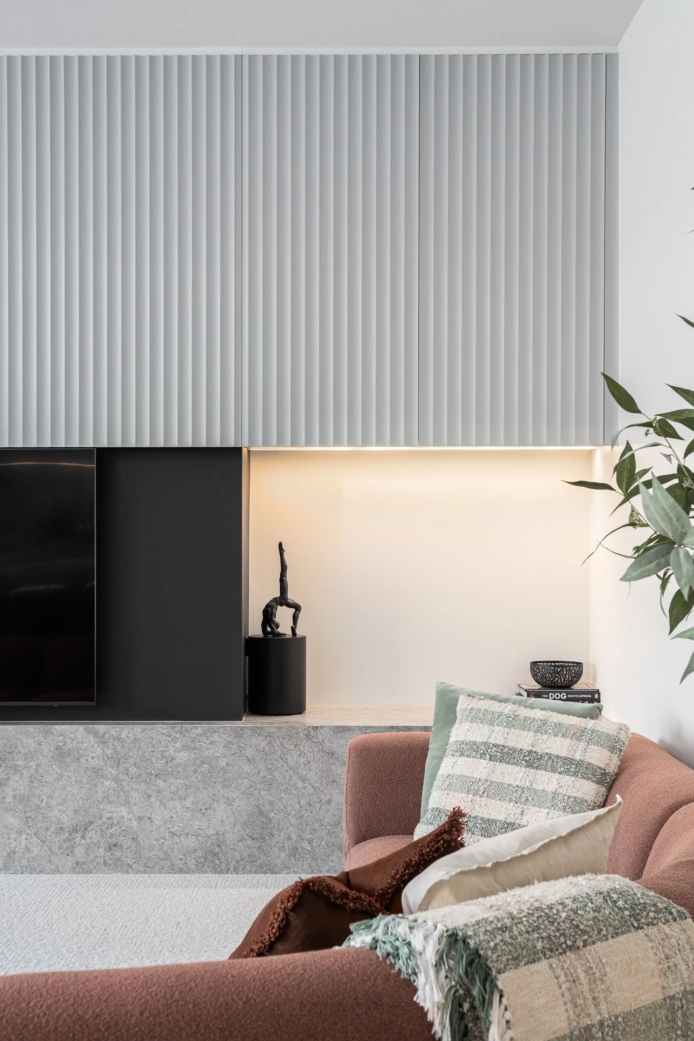 Modern living room with a flat-screen TV, artwork, and decorative pillows on a pink sofa.