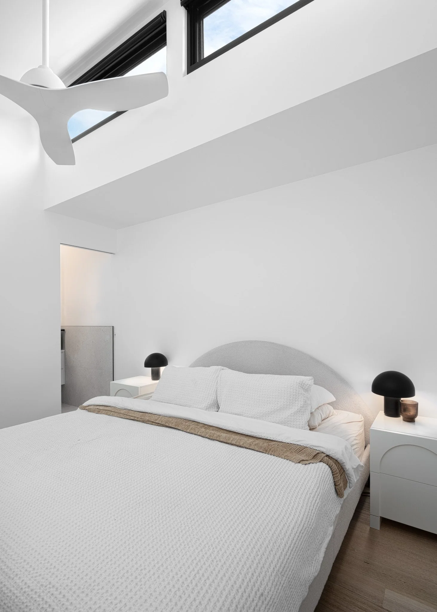Minimalist bedroom with white bedding, black bedside lamps, and a sloped skylight window.