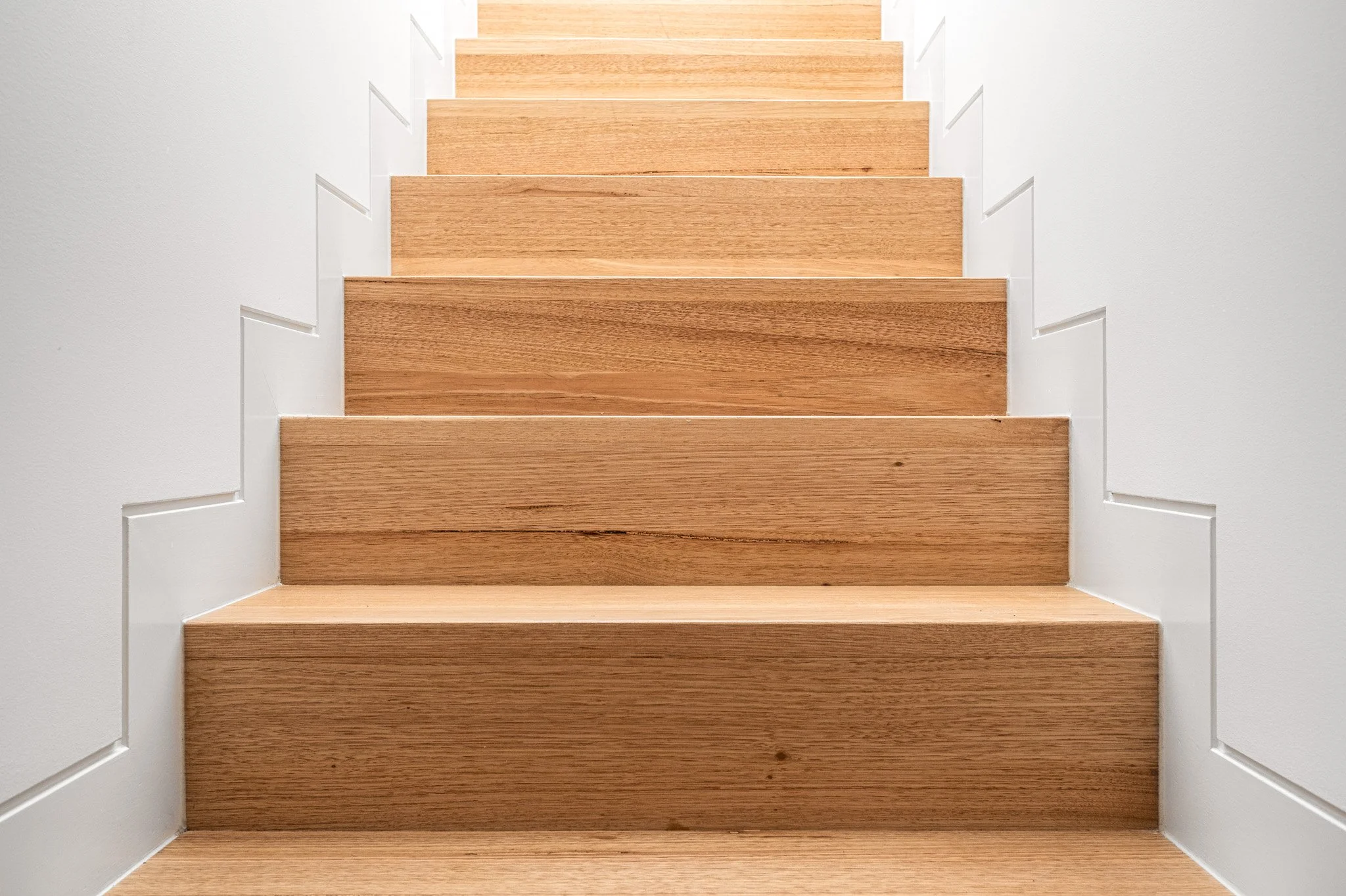 Wooden staircase with white walls on each side.