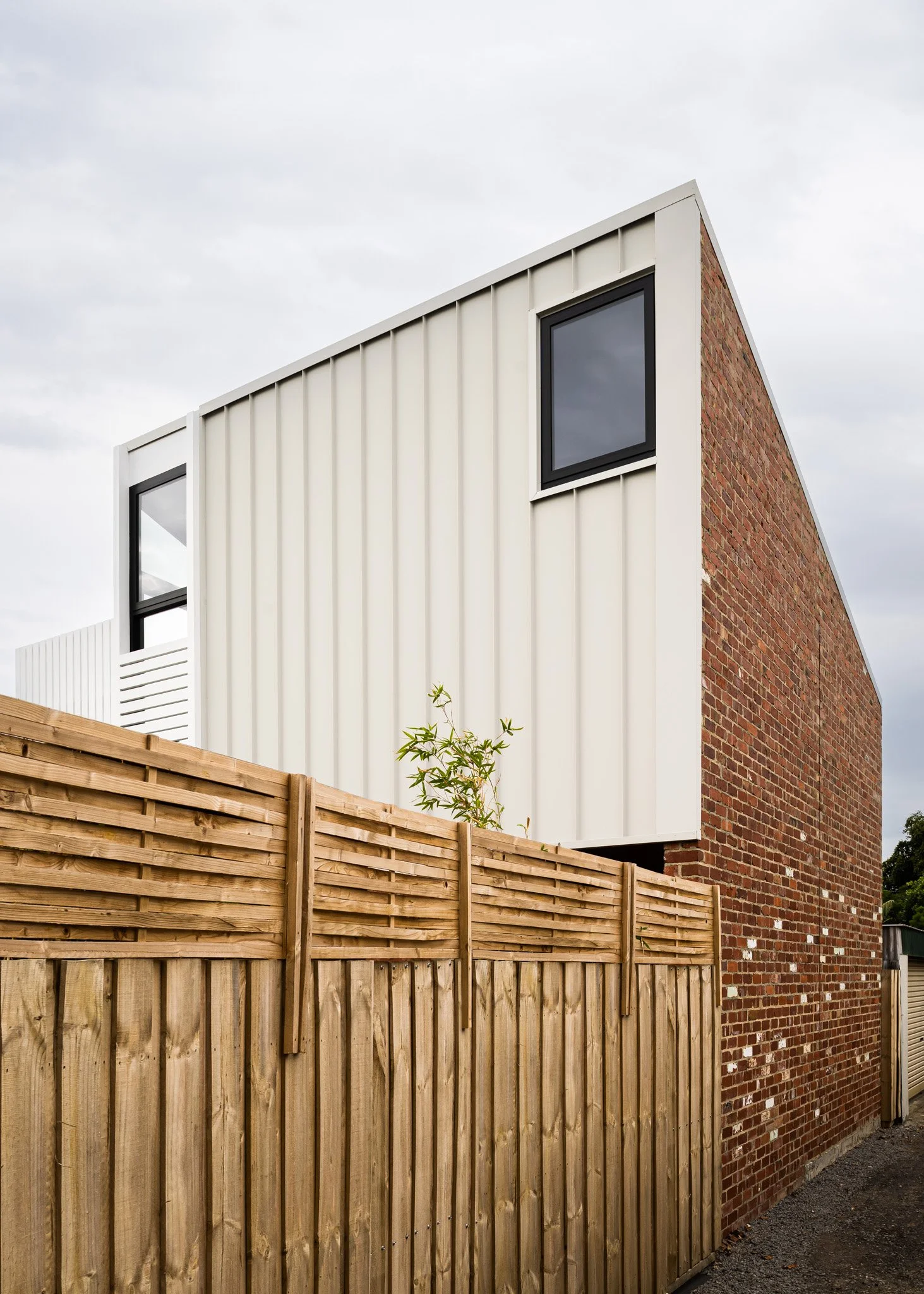 Modern two-story house with brick and white metal siding, black-framed windows, and a wooden privacy fence in front.