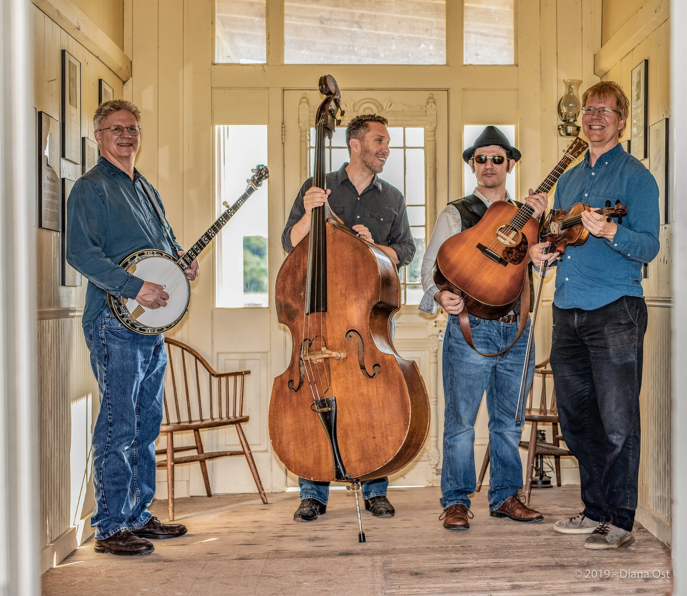 Hot Pickin 57s bluegrass band posed with banjo, upright bass, guitar and fiddle in a doorway at Pioneer Farms, Austin