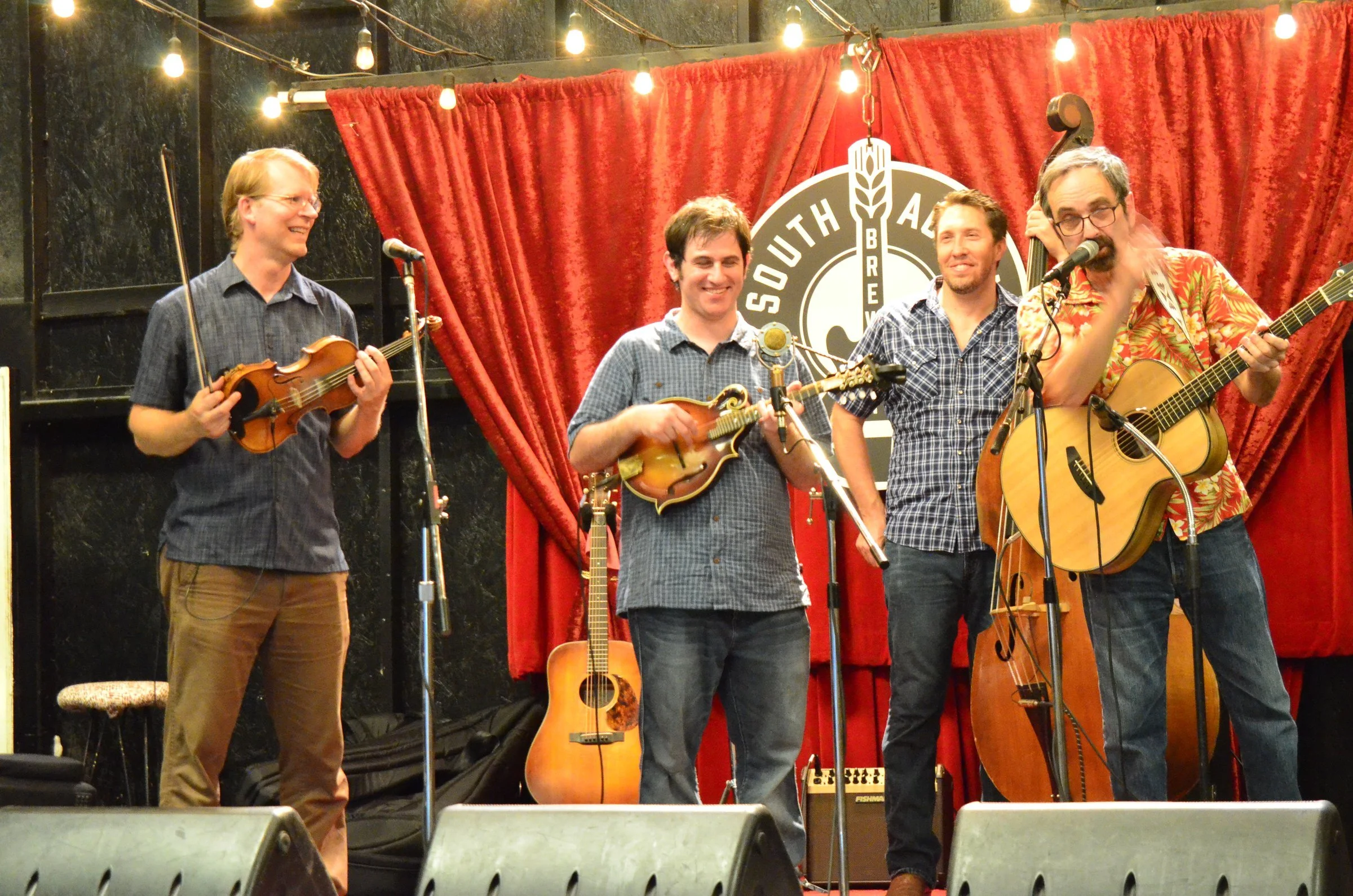 Hot Pickin 57s laughing on stage at South Austin Brewery with a red curtain and brewery logo behind them