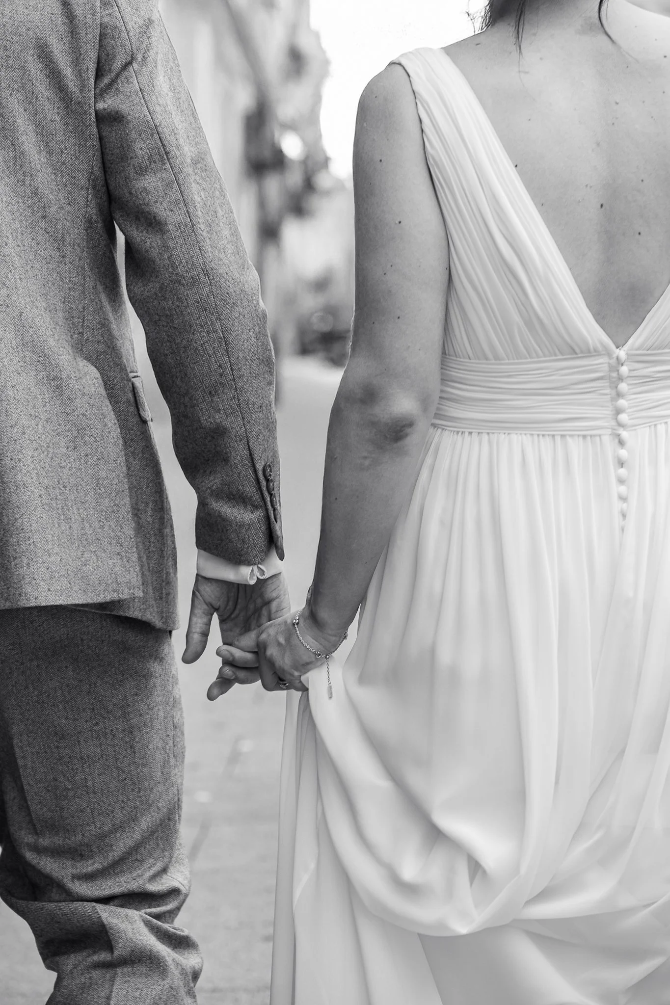 Image from behind of Bride and Groom Holding hands walking Brighton Streets. Blacka nd White, Close up.
