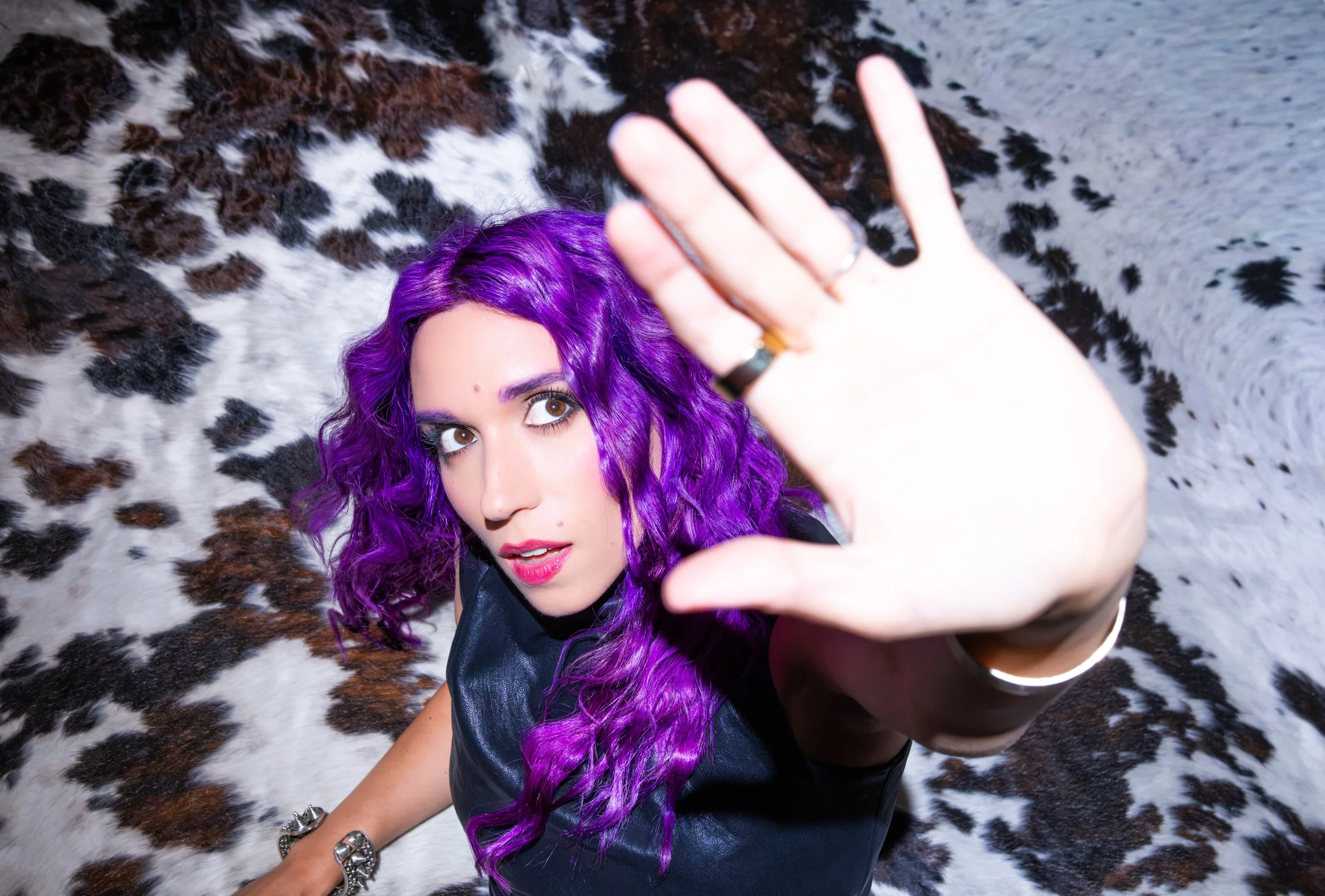 Woman with vibrant purple hair taking a selfie while lying on a cowhide rug with black, white, and brown spots.