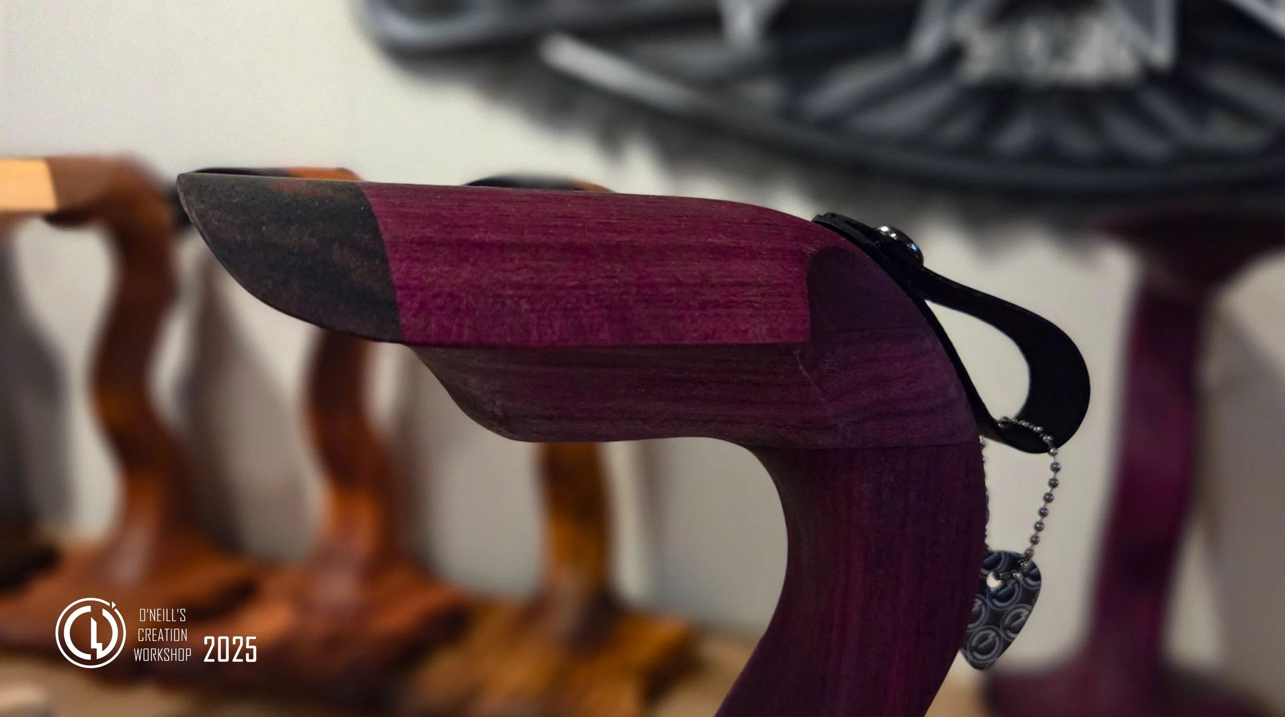 Close up of the head of a gorgeous purpleheart grumpy goose headphone stand with blurred grumpy gooses in the background and hand carved sign