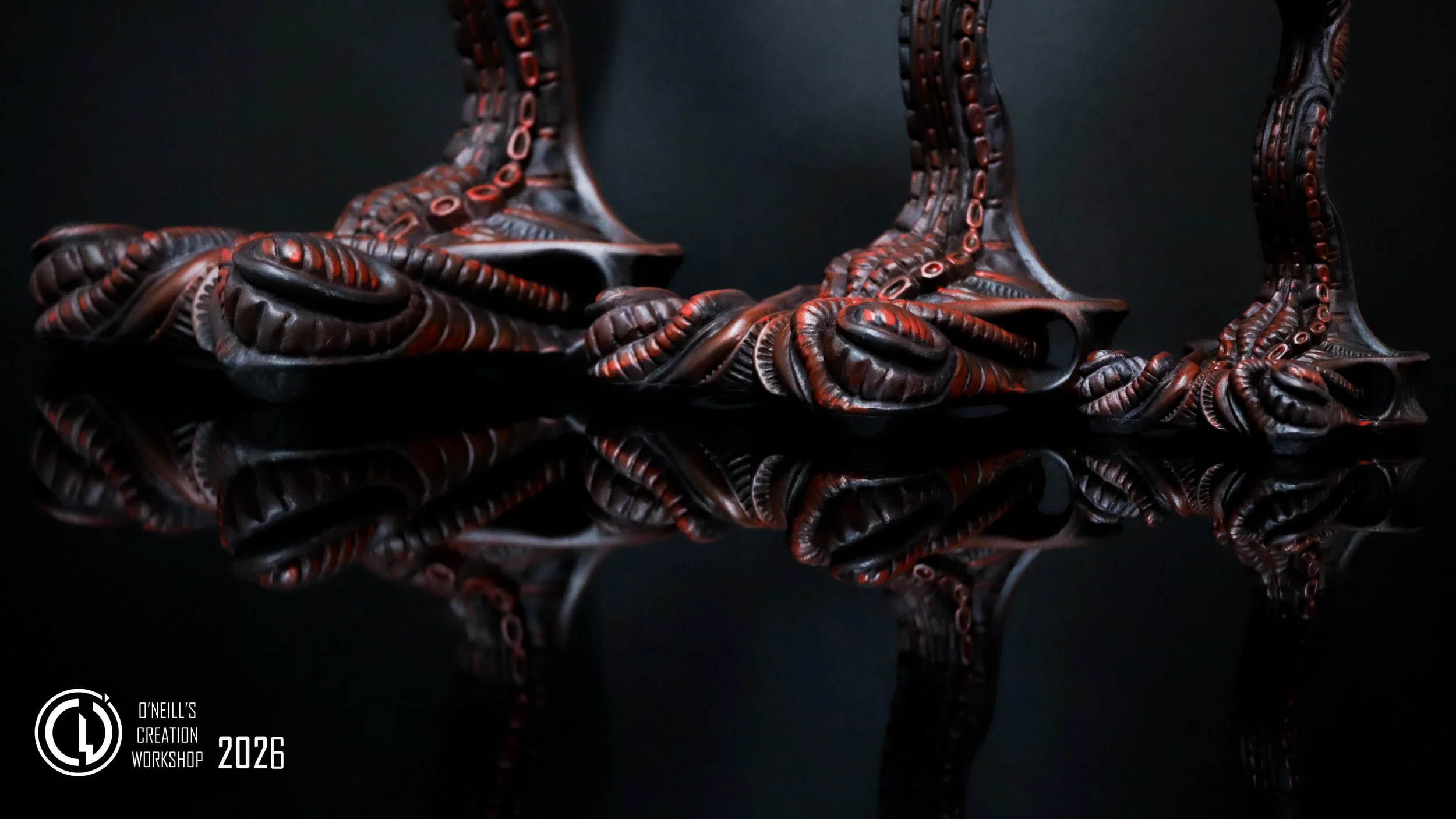 three 3D Printed Grumpy Goose Headphone Stands, hand painted in a dark red tone, they are all identical and have a biomechanical theme in there design, their buildO'Neill's Creation Workshop Logo is overlaid in bold white in the bottom left corner.