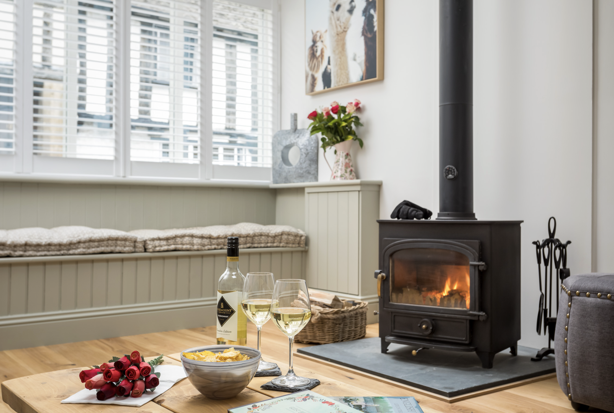A cozy living area at The Bolt Hole in Winchcombe, featuring a warm log burner, comfortable seating, and a glass of wine on a table