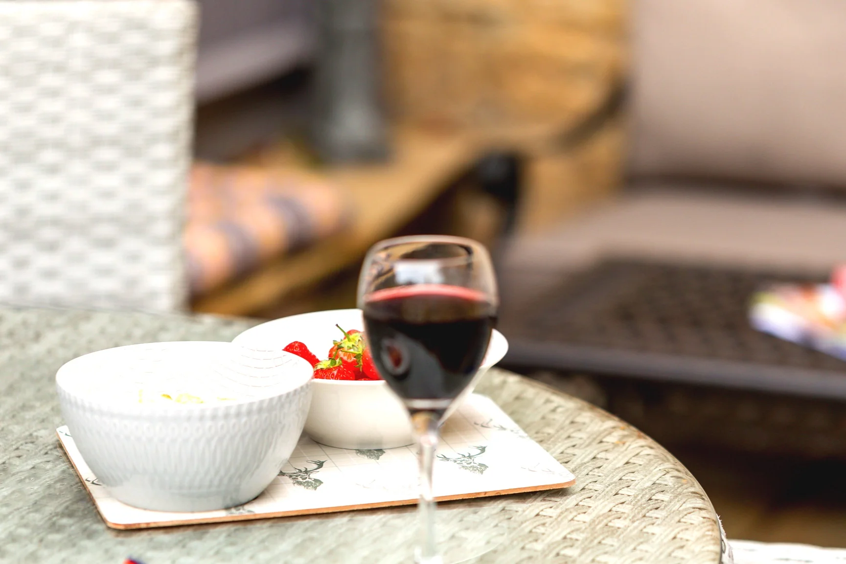 An inviting outdoor table setting featuring a glass of red wine, a bowl, and snacks, perfect for a relaxing evening at the cottage