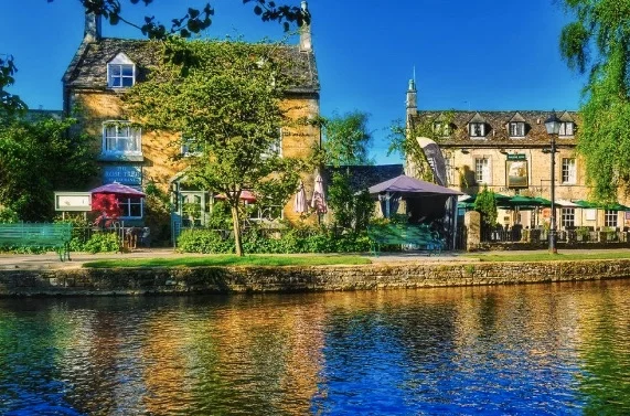 A scenic view of historic stone buildings along the riverbank in Bourton-on-the-Water, highlighting the beautiful local setting for market days
