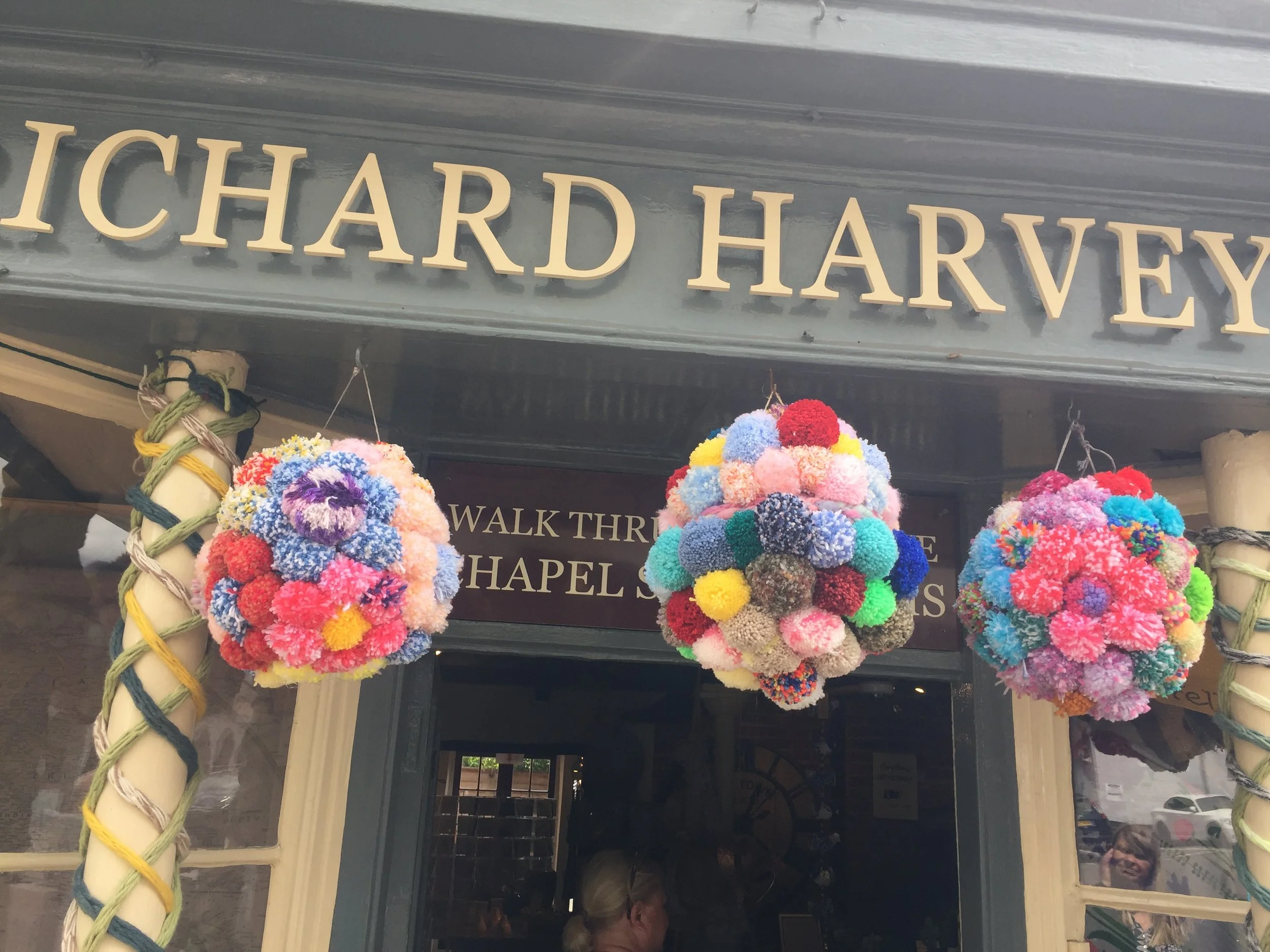 Vibrant, handmade pom-pom decorations hanging in front of a shop entrance, reflecting the festive spirit of the local community
