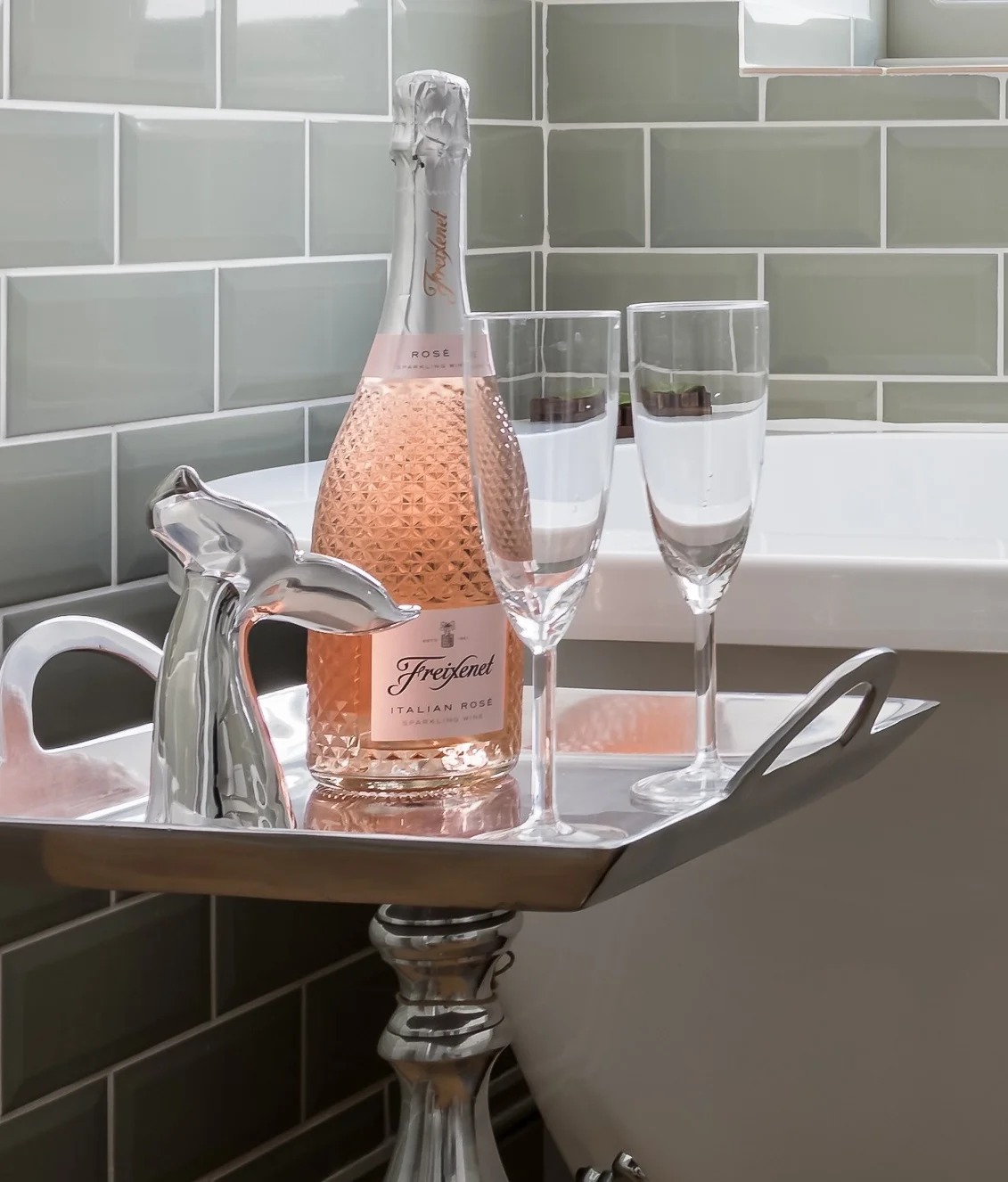 Luxury welcome setup at The Bolt Hole cottage in Winchcombe featuring a silver tray with a bottle of champagne and two glasses next to a tiled wall