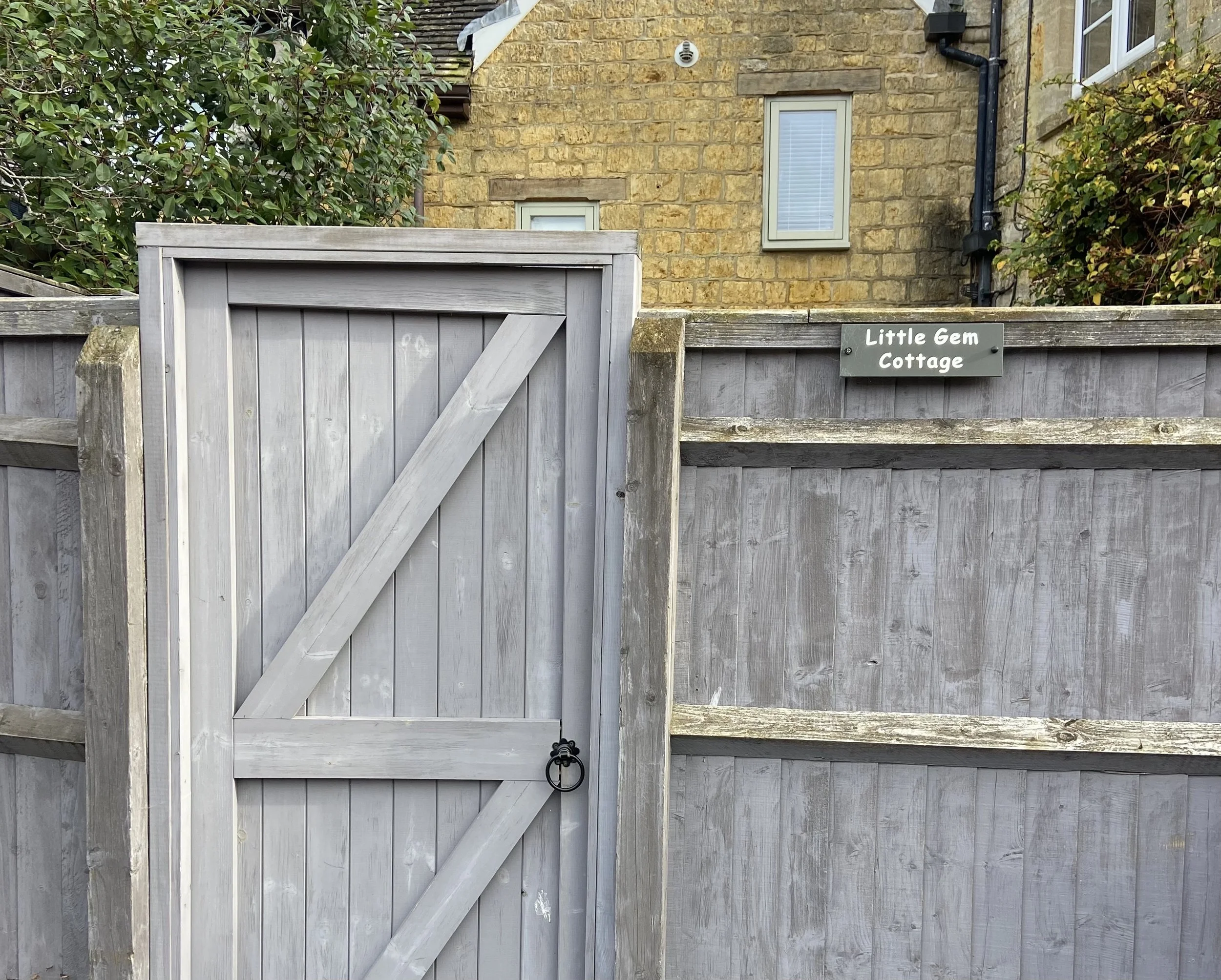 Grey wooden back garden gate and fence for Little Gem Cottage in Bourton-on-the-Water, featuring a small black sign on the fence that reads 'Little Gem Cottage'