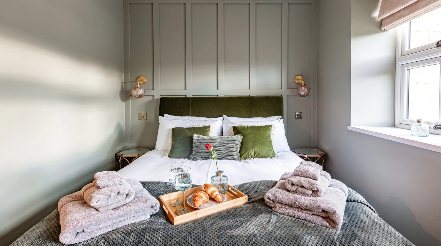 A master bedroom at Hideaway Cottage, featuring elegant wood panelling, a comfortable bed with plush linens, and a welcome tray.