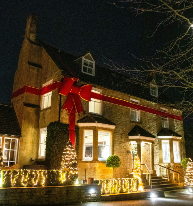 A stone building at night, Dormy House, decorated with a large red ribbon bow and warm festive lights for the Christmas season