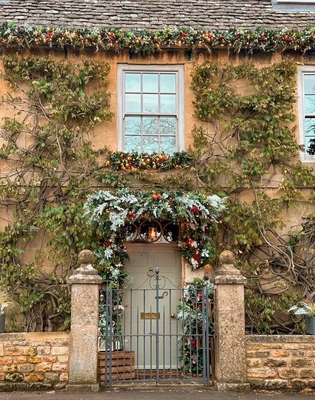 A festive, ivy-covered stone cottage entrance decorated for the holidays, perfectly capturing the magical atmosphere of the Stow-on-the-Wold Christmas Tree Festival