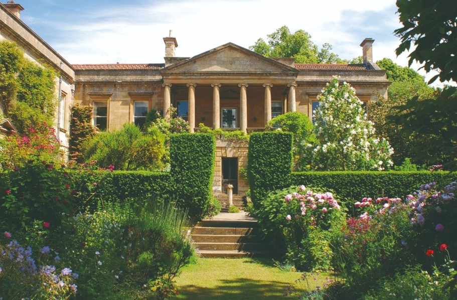 A scenic view of the historic Kiftsgate Court house surrounded by lush, vibrant gardens, featuring the famous Kiftsgate rose