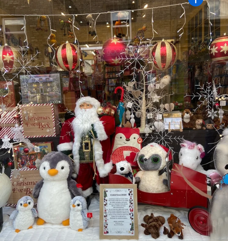 A festive shop window display in Stow-on-the-Wold featuring Christmas decorations, including Santa Claus, plush toys, and twinkling lights