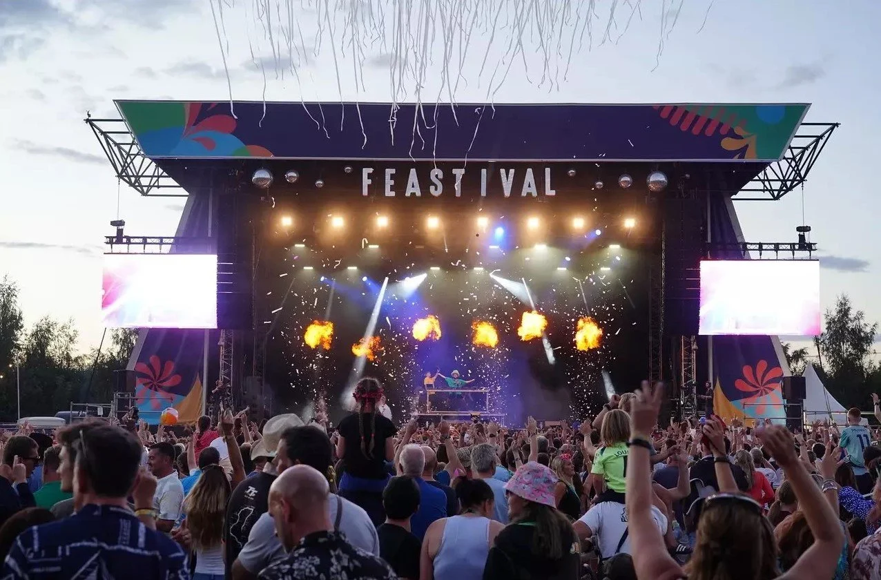 A large, excited crowd watching a musical performance on the main stage at The Big Feastival, set against a backdrop of trees