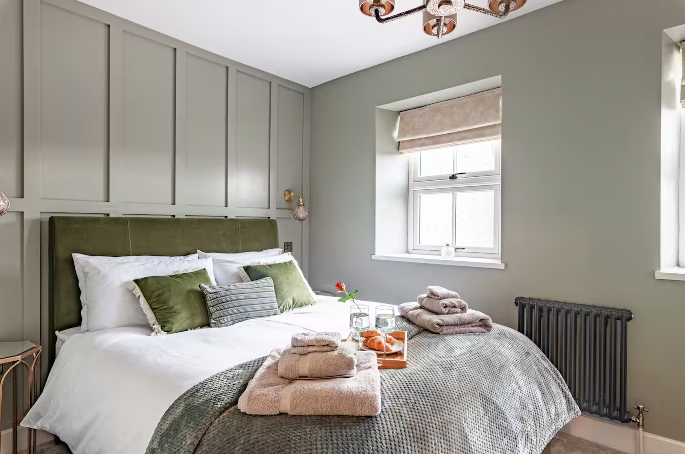 A cozy, well-decorated bedroom at Hideaway Cottage in Bourton-on-the-Water, featuring modern green wall paneling, comfortable bedding, and a breakfast tray