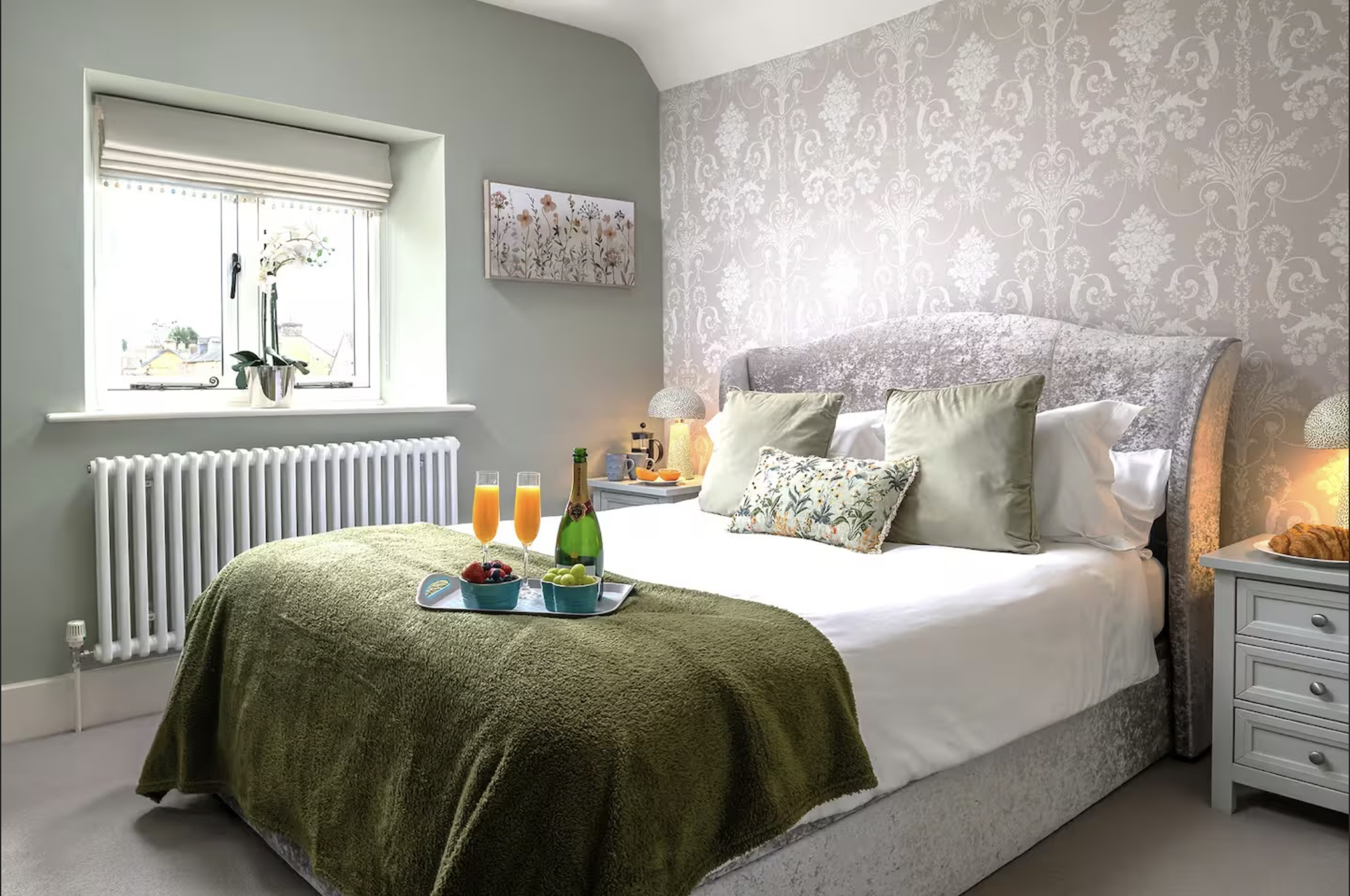 A charming, newly renovated bedroom at Little Gem Cottage, featuring elegant patterned wallpaper, crisp white linens, and a welcoming breakfast tray set on the bed